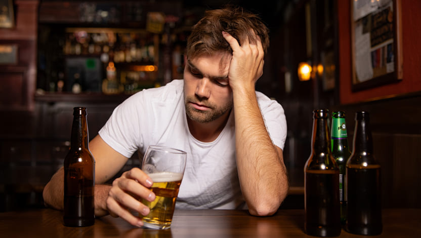 Мужчина, борющийся с пивной зависимостью, за столом в окружении пустых бутылок